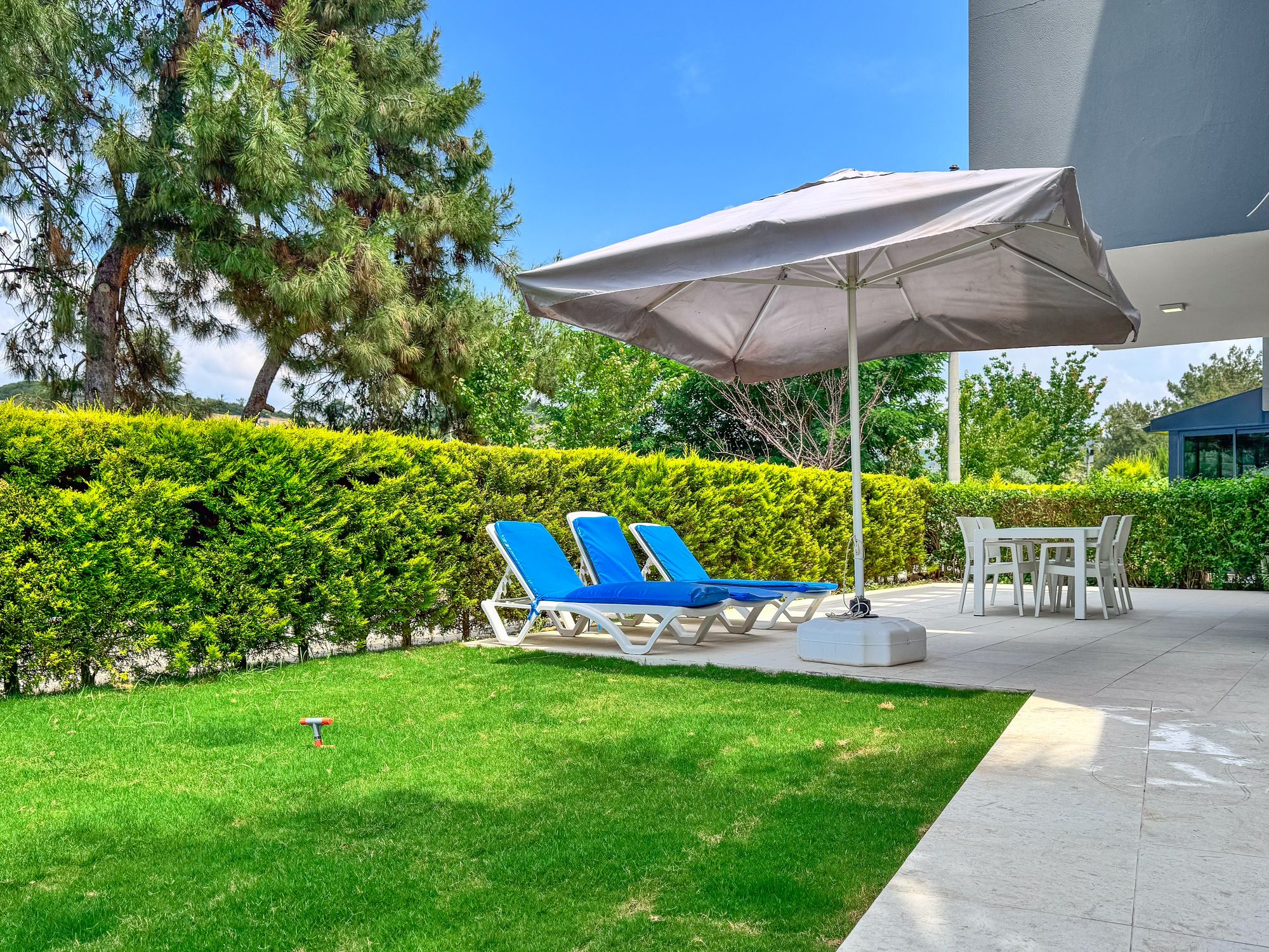 Private garden terrace with sun loungers under a large parasol, lawn and outdoor dining set framed by pines