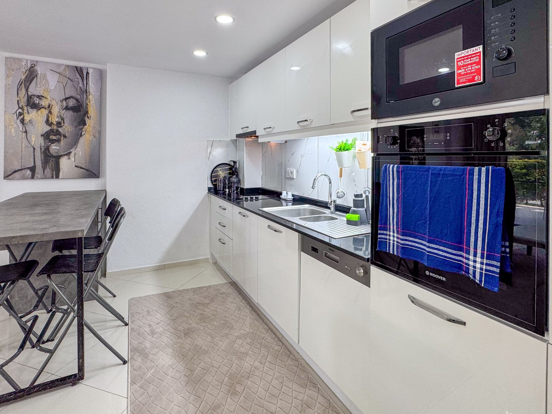Modern galley kitchen with white high-gloss cabinetry, dark stone counters, oven and dishwasher