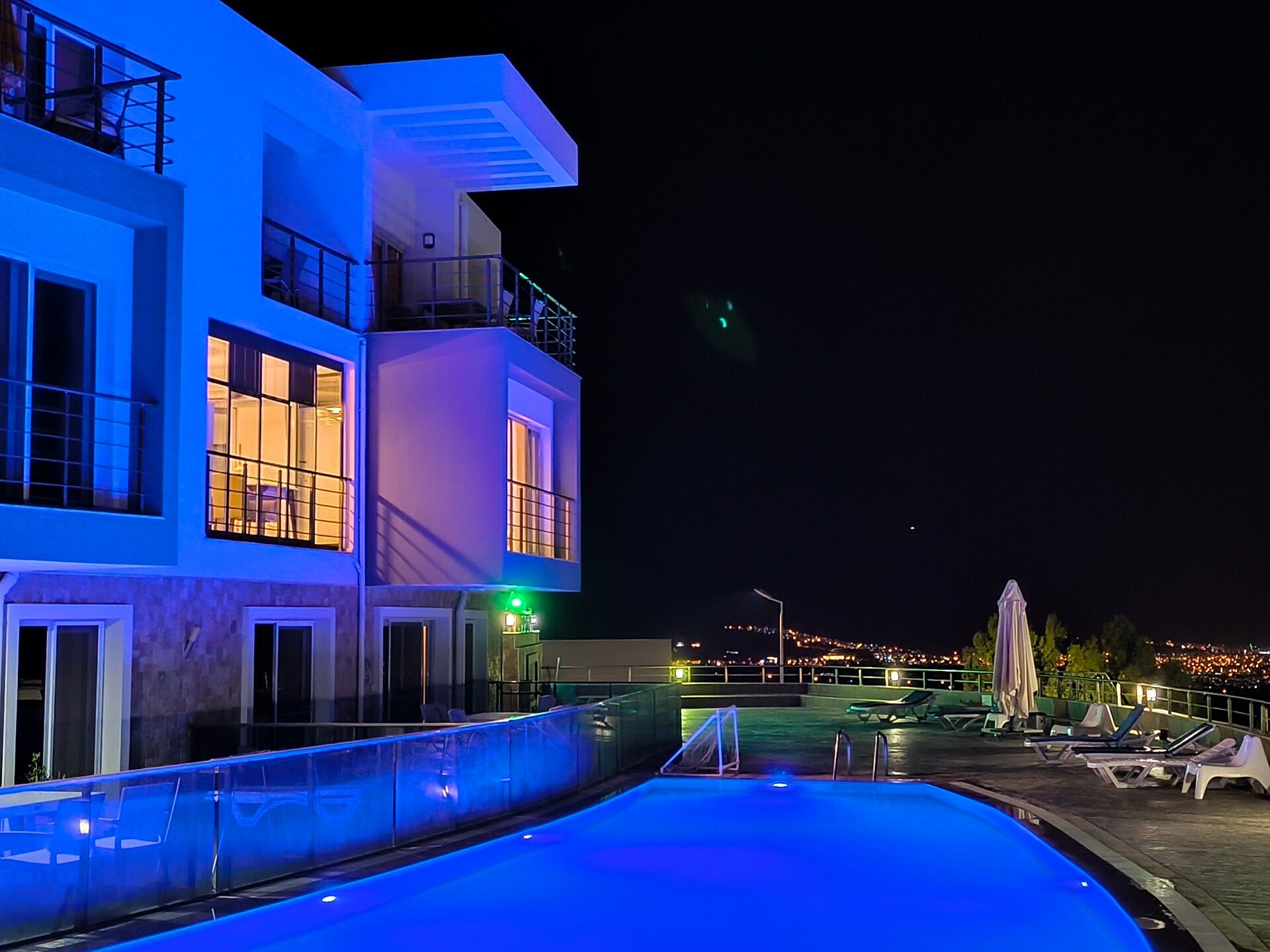 Pool deck at night with the city of Kuşadası lit in the distance