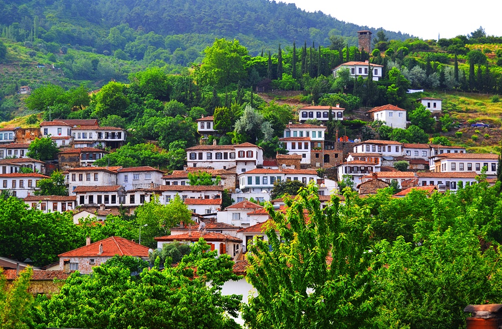 Whitewashed stone houses with terracotta roofs cascading down the green hillsides of Şirince village