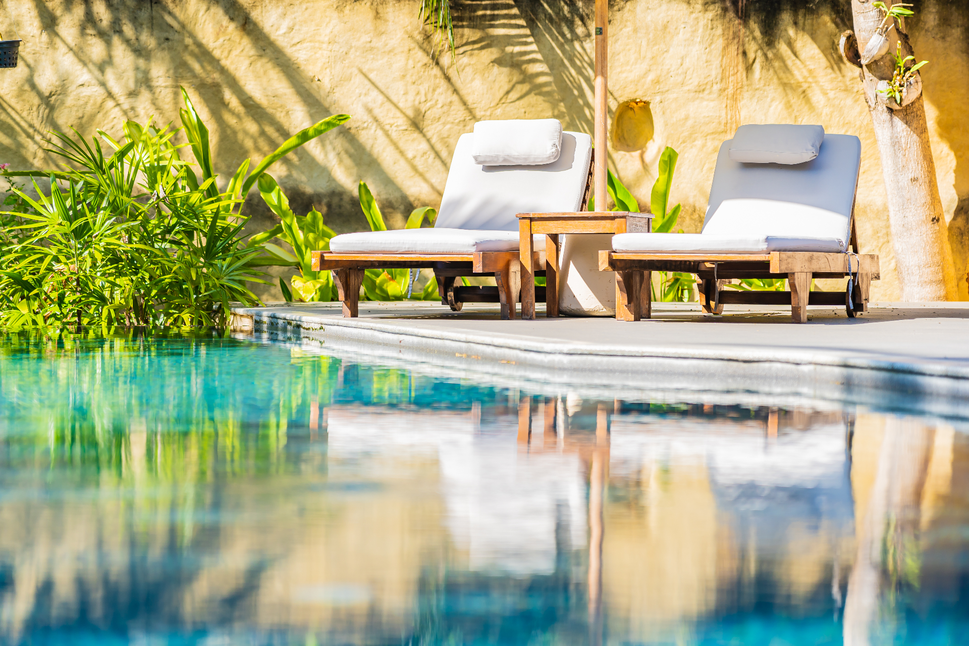 Two sun loungers and a parasol beside a private villa pool surrounded by tropical plants